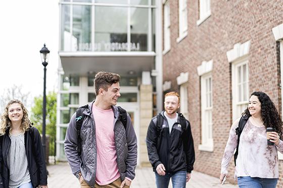 Photo of four Chatham University 学生 leaving an academic building after class, 边走边聊. 